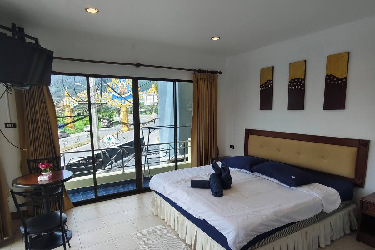 Quarto de hotel com cama, televisão, varanda e vista, e área de refeições com mesa e cadeiras.