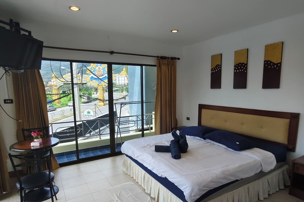 Habitación de hotel con cama, televisión, balcón con vistas y zona de comedor con mesa y sillas.