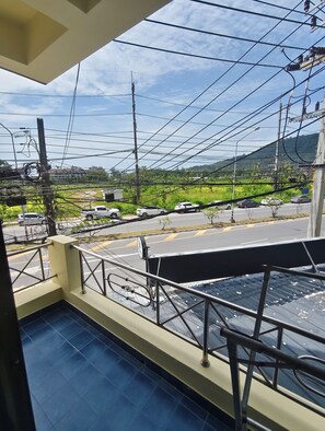A balcony with a view of a road, power lines, and distant buildings. - Kamala Cool 2 (Kamala)