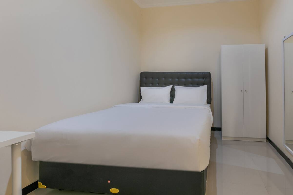 A small, neatly arranged bedroom with a single bed, a white wardrobe, and a small table.