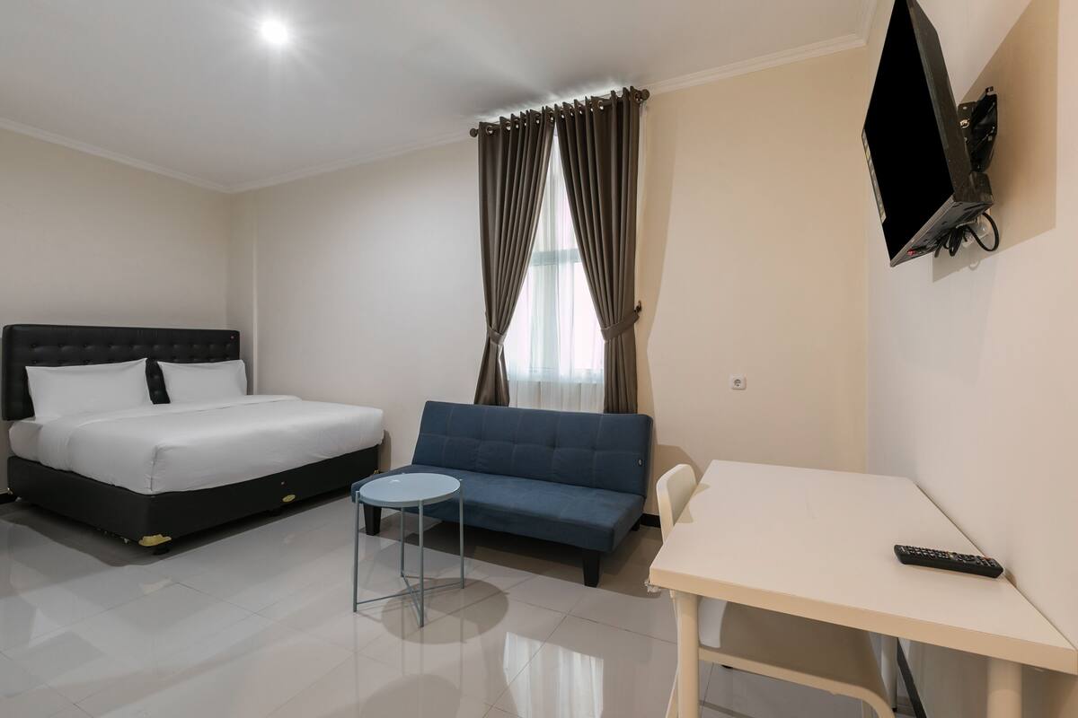 A hotel room with a bed, a sofa, a small table, and a TV mounted on the wall.