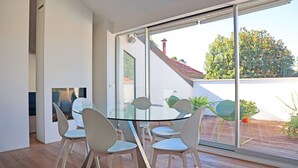 A modern dining area with a glass table and white chairs, large windows, and a view of a garden and building outside. - Castello Charme Style House (Milano)