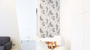 Un espace repas moderne avec une table et des chaises blanches, un canapé noir et une porte à motifs.