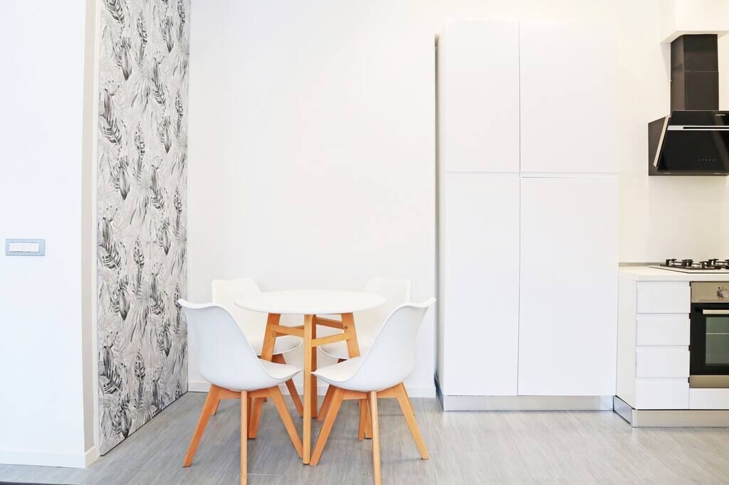 A modern kitchen with white cabinetry, a black range hood, and a white dining table with four chairs.
