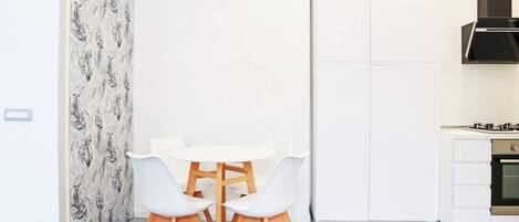 A modern kitchen with white cabinetry, a black range hood, and a white dining table with four chairs.