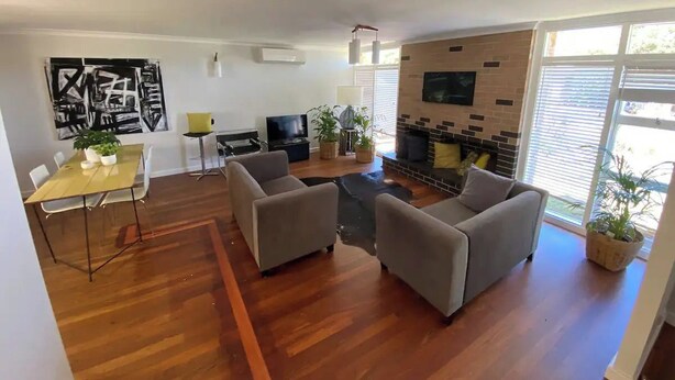Un soggiorno con pavimento in legno, divani grigi, una TV, un caminetto e un'area pranzo con tavolo e sedie.
