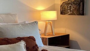 Un letto rifatto con cuscini bianchi e marroni, una lampada da comodino e un quadro appeso al muro.