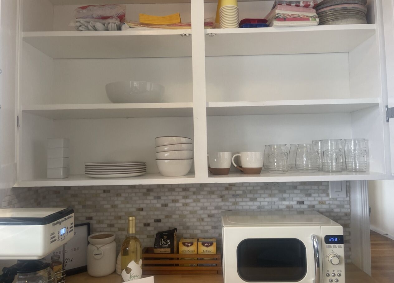 Eine Küche mit weißen Schränken, einer Mikrowelle, einer Kaffeemaschine und diversen Küchenutensilien.