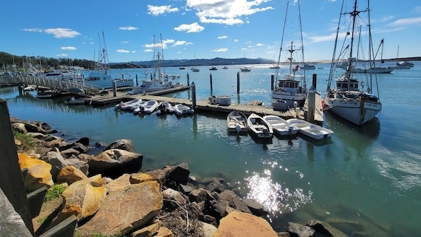 Eine Marina mit an Holzstegen vertäuten Booten, umgeben von felsigen Ufern und blauem Himmel.