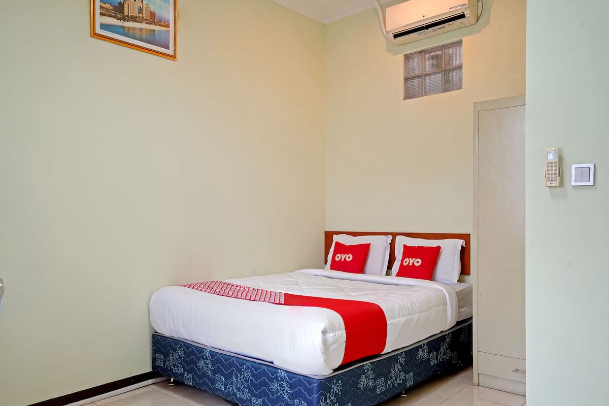 Een hotelkamer met een bed, een wandairconditioner, een klein raam en een deur.