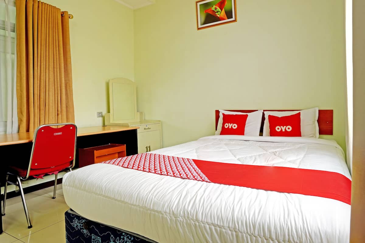 Een hotelkamer met een bed, een bureau, een stoel, een dressoir en een schilderij aan de muur.