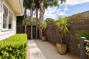 A paved patio with a low wall, potted plants, and a wooden fence.
