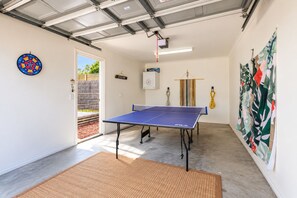 A ping pong table in a room with a door leading outside, a dartboard, and a colorful abstract painting on the wall.