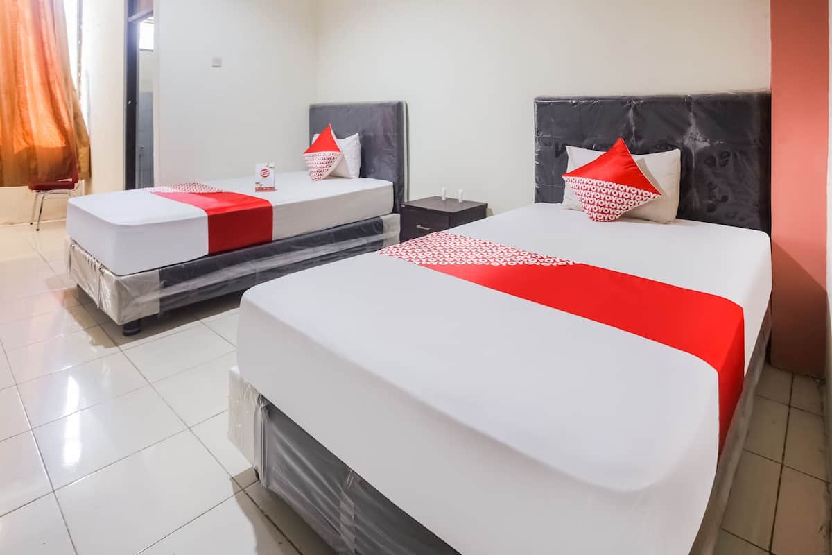 Habitación de hotel con dos camas, cada una con colcha y almohadas rojo y blanco. El piso es de baldosas y hay un espejo grande en una pared.