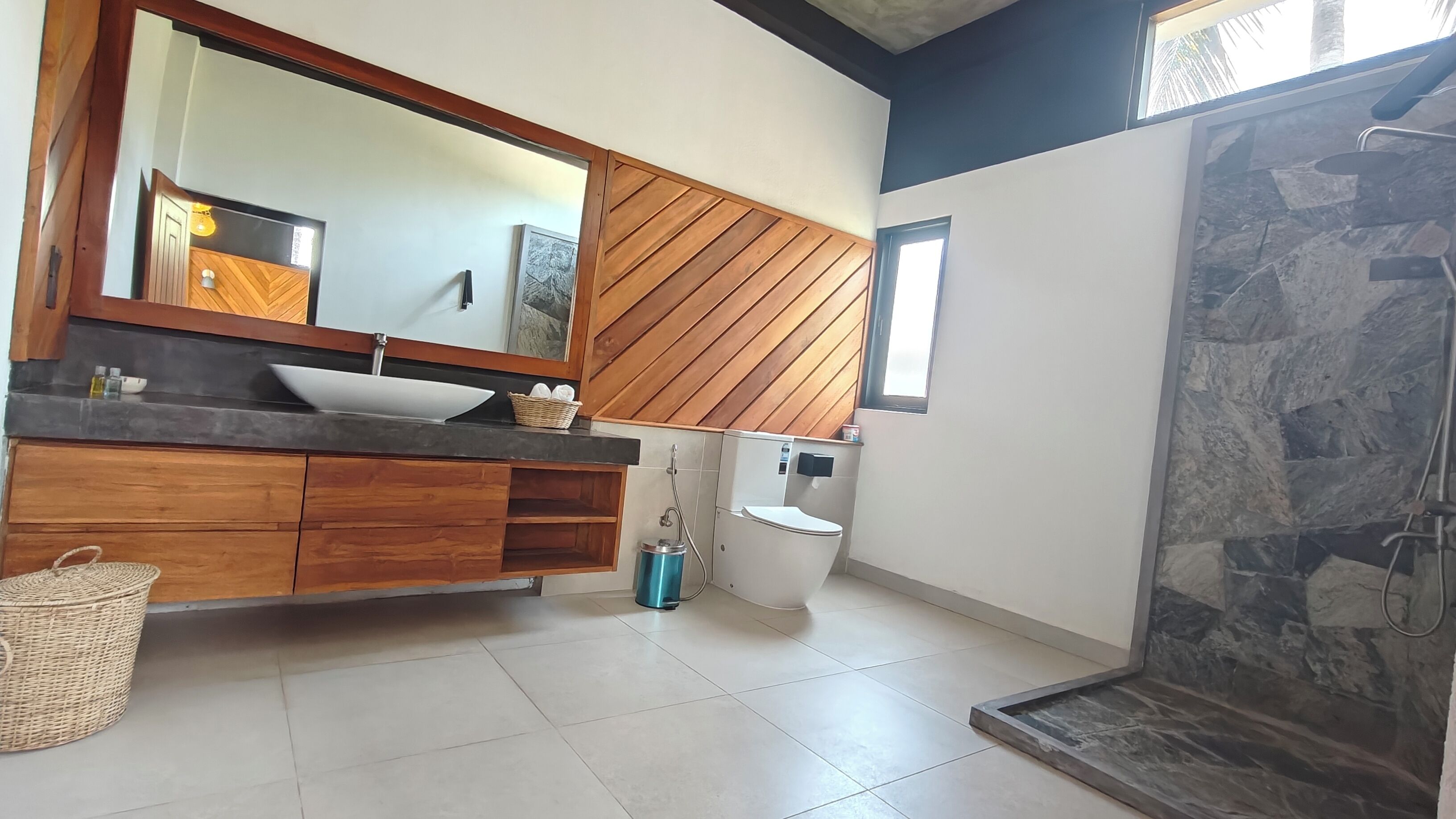 Un baño moderno con tocador de madera, un espejo grande, un lavabo blanco, un inodoro y una zona de ducha.