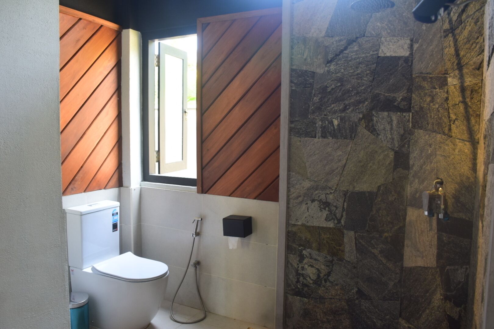 Un bagno con il water, doccia e una finestra con persiane di legno.