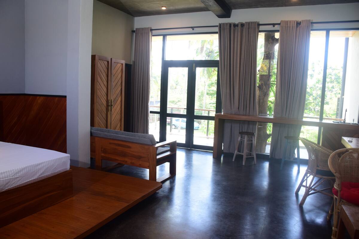 A room with a bed, a desk, and a chair. There is a window with curtains.