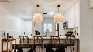 Una cocina con una isla central, dos lámparas colgantes de mimbre y una zona de comedor con cuatro sillas de mimbre.