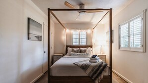 Una cama con dosel, un cabecero, una mesita de noche con una lámpara y una ventana con persianas.