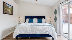 A bedroom with a large bed, a ceiling fan, two bedside lamps, a window with curtains, and a wall-mounted decorative item. - Private home near Zion & state parks, BBQ, cozy stay for family & friends in scenic red rock views! (La Verkin)