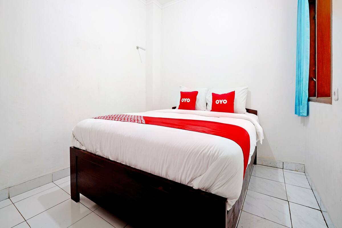 Une chambre à coucher avec un lit, des murs blancs, une tête de lit en bois et une couvre-lit rouge et blanche.