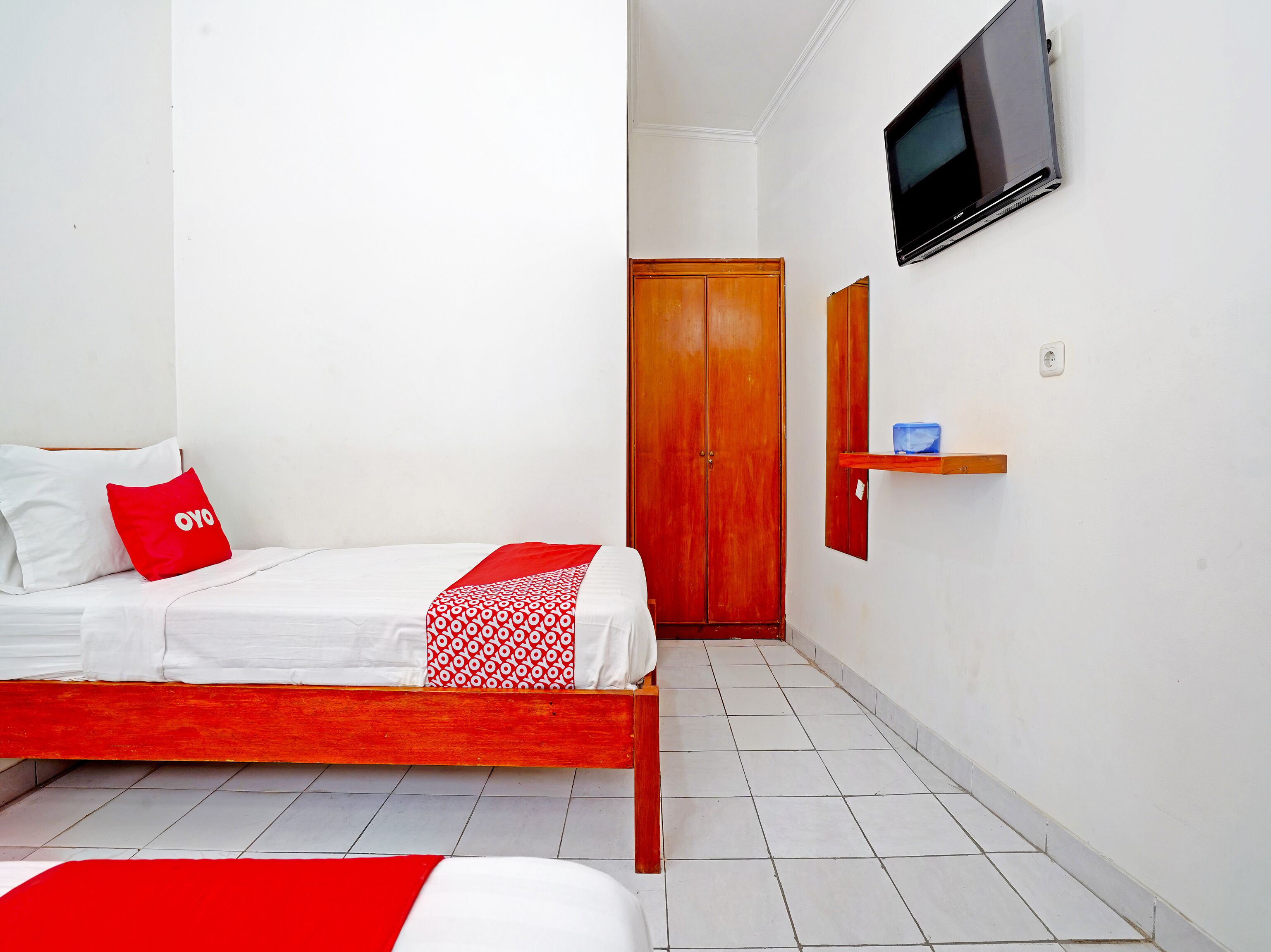 A hotel room with a bed, a TV mounted on the wall, and a wooden wardrobe.