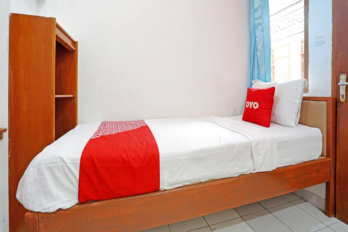 Un lit simple avec une couvre-lit rouge et blanche, une tête de lit en bois et un oreiller rouge sur lequel est inscrit le mot « OYO ».