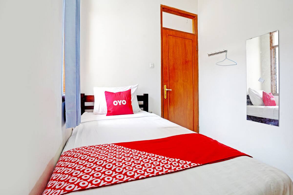 Une chambre d’hôtel avec un lit, une porte en bois, un mur blanc et un miroir.
