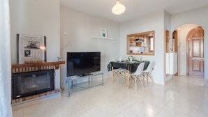 A modern living room with a fireplace, a flat-screen TV, a dining table with chairs, and a kitchen area visible through an archway. - Magnificent Casa Azahara (Mont-roig del Camp)