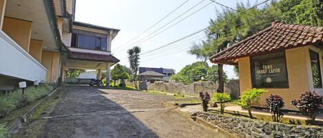 Une rue résidentielle bordée de maisons, un petit bâtiment portant l’inscription « TAMU HARAP LAPOK » et un chemin de terre.