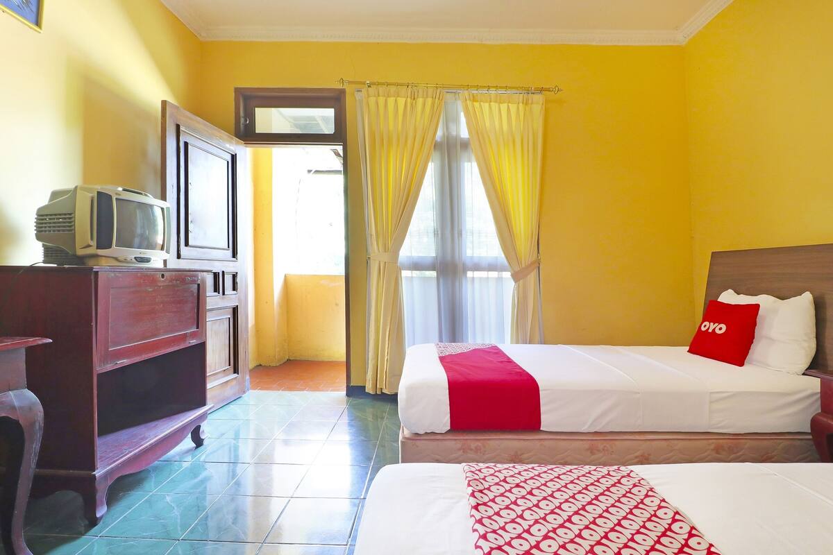 A hotel room with a bed, a TV, a wooden cabinet, and a window with curtains.