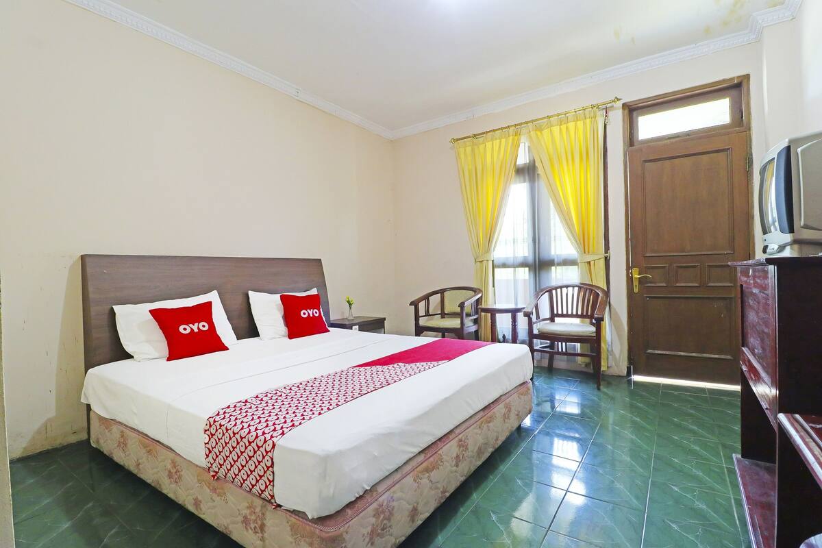 A hotel room with a bed, a television, a wooden door, and a window with yellow curtains.