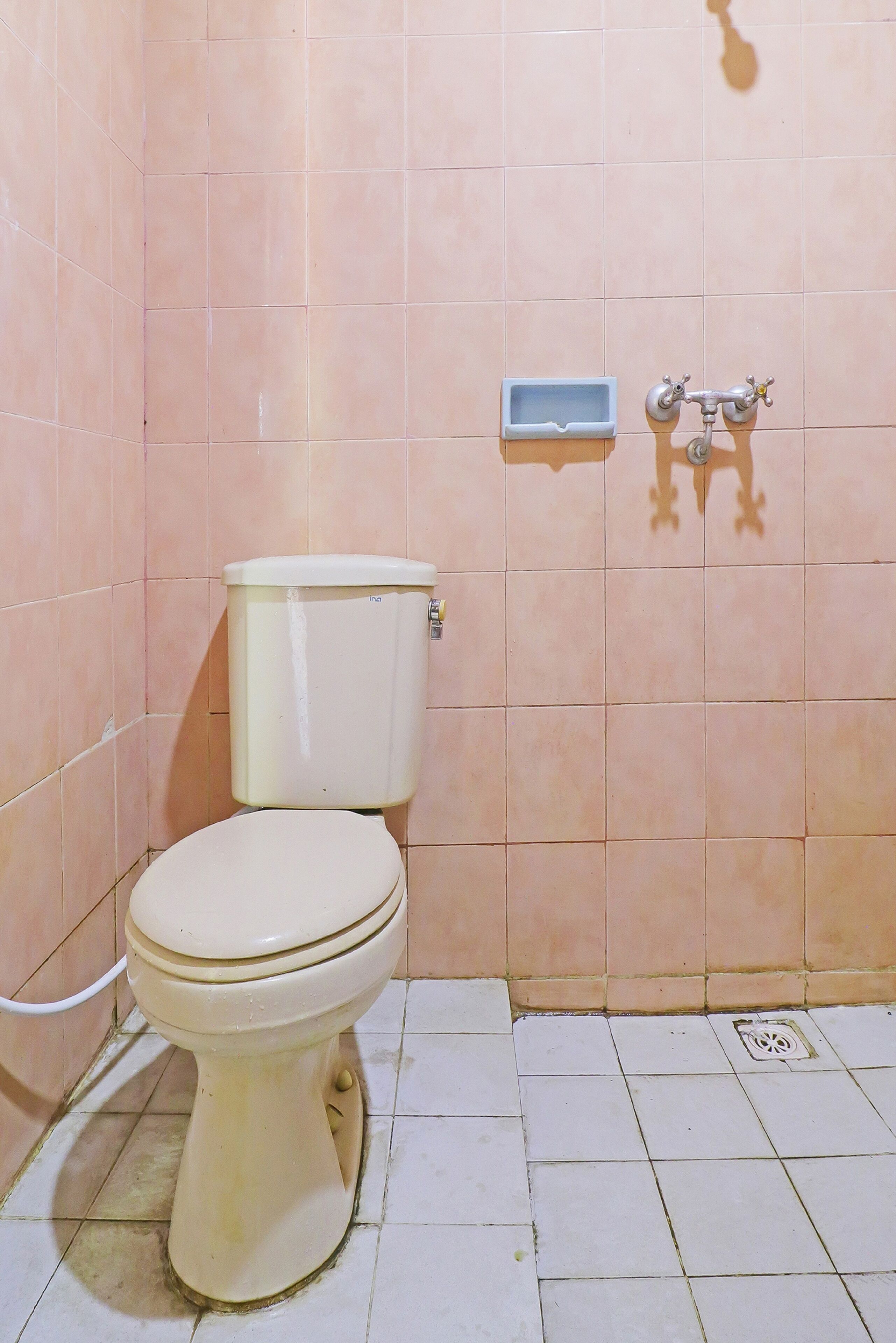 Casa de banho pequena e simples, com sanita, lavatório fixo e chuveiro.