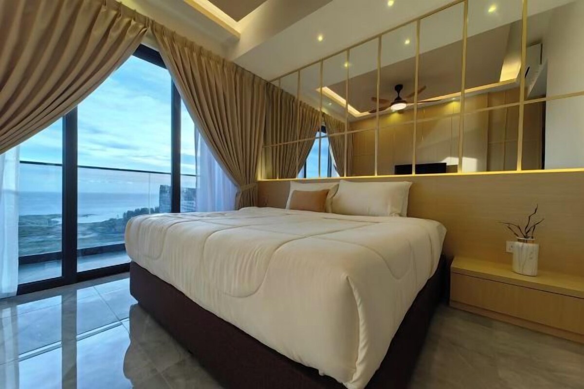 A modern bedroom with a large bed, a view of the ocean, and a ceiling fan.