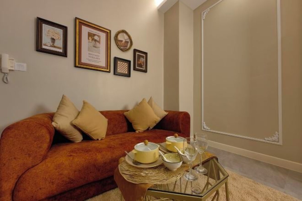 A living room with a sofa, cushions, a glass coffee table with dishes and glasses, and framed pictures on the wall.