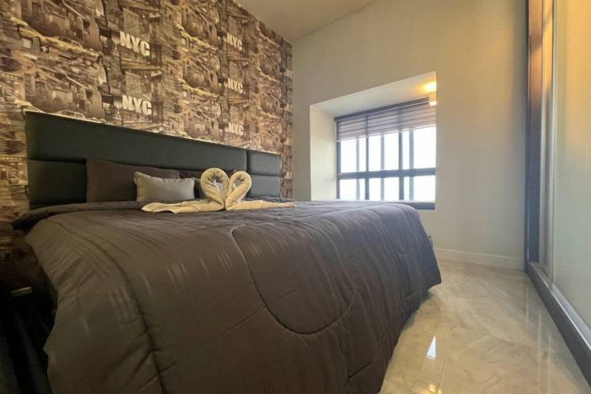 A bedroom with a large bed, a stone-patterned wall, a window with blinds, and a small skylight.