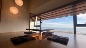 A modern room with a large window overlooking the sea, a wooden floor, and a table with cushions. - Attic Home Melaka Imperio Residence (Malacca City)