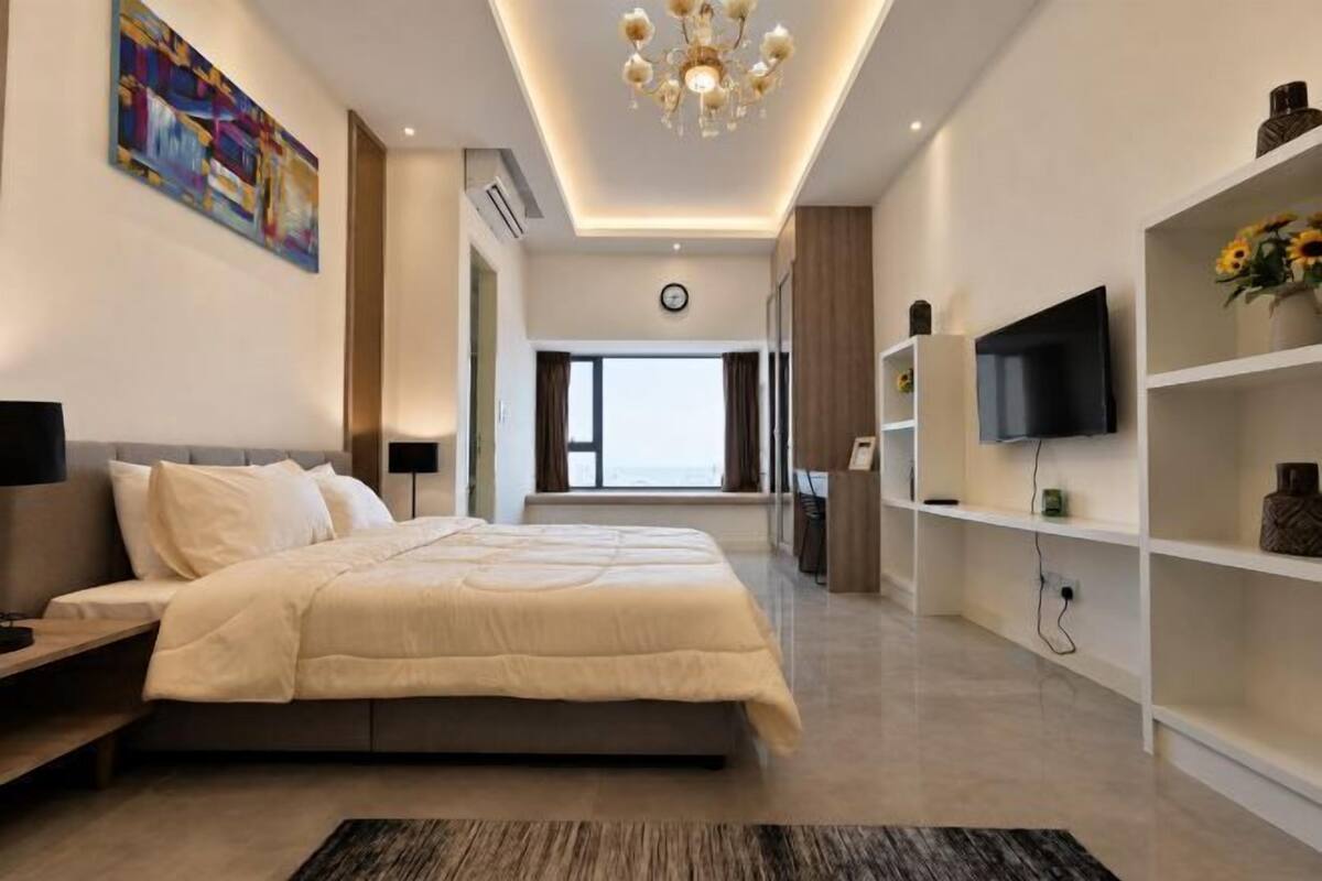 Un dormitorio moderno con una cama grande, un televisor, una estantería y vistas al exterior.