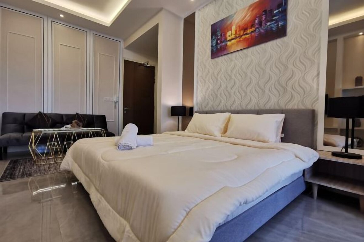A modern hotel room with a large bed, a sofa, a desk, and a painting on the wall.