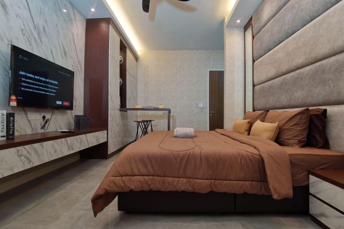 A modern bedroom with a large bed, a television on the wall, and a small desk area.