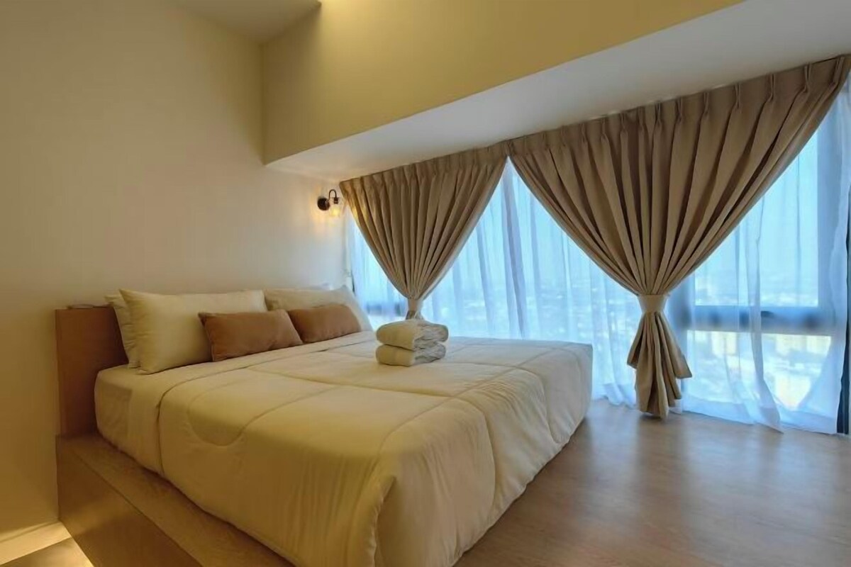 A modern bedroom with a large bed, beige curtains, and a city view.