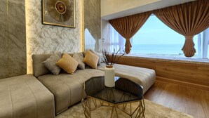 A modern living room with a sofa, a glass coffee table, and a view of the sea through large windows. - Attic Home Melaka Imperio Residence (Malacca City)