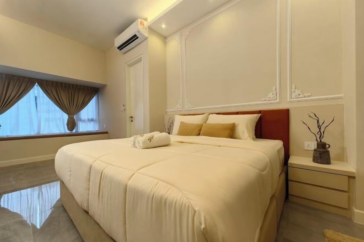 A neatly made bed with a white comforter and pillows, a bedside table with a vase, and a window with curtains.