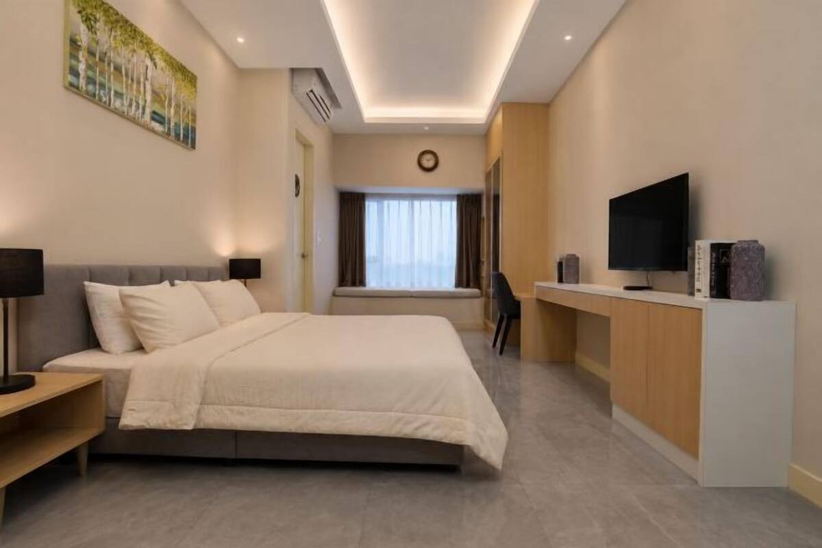 Una habitación de hotel moderna con cama, mesita de noche, escritorio, televisor y un cuadro en la pared.