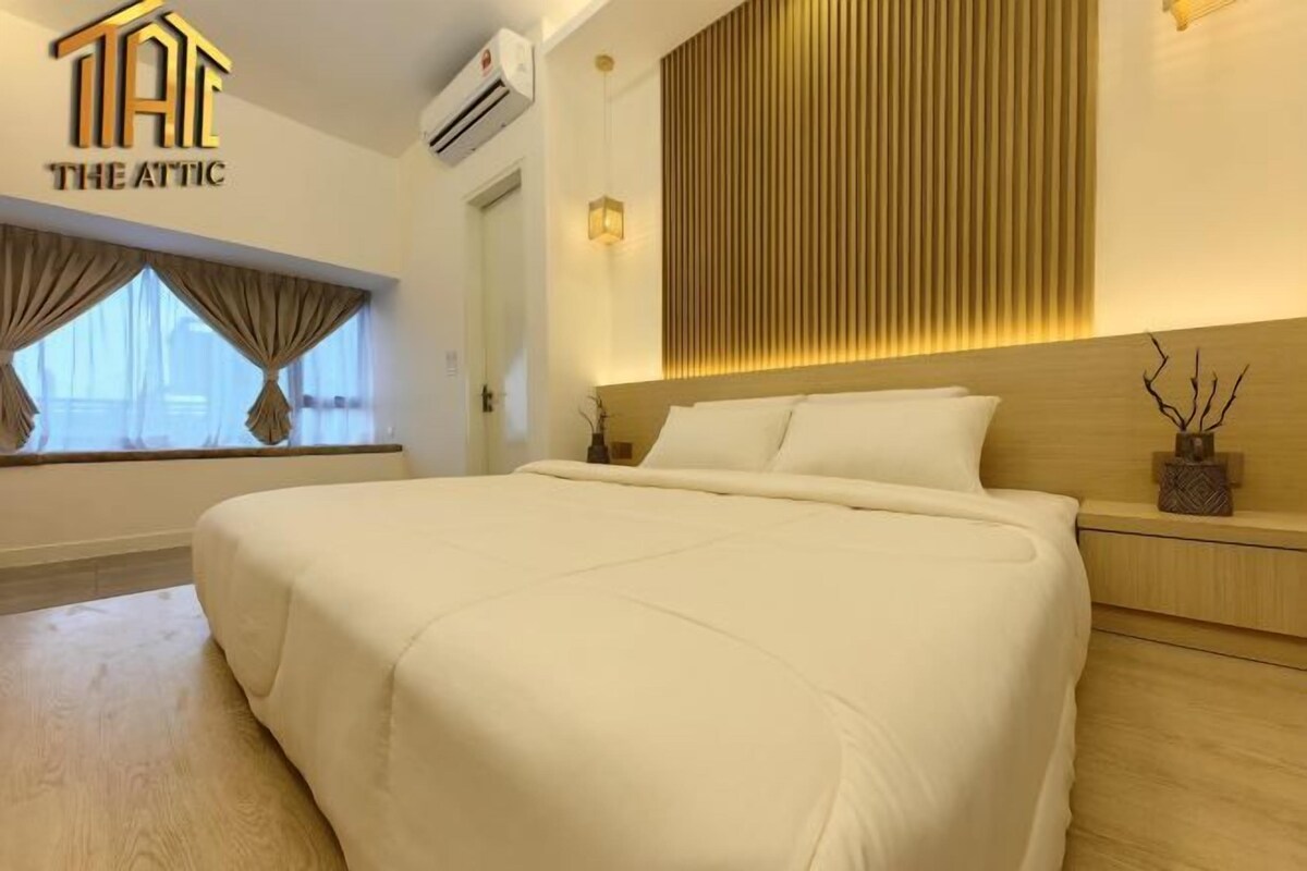 A hotel room with a large bed, a window with curtains, a wall-mounted air conditioner, and a wooden panel design on the wall.