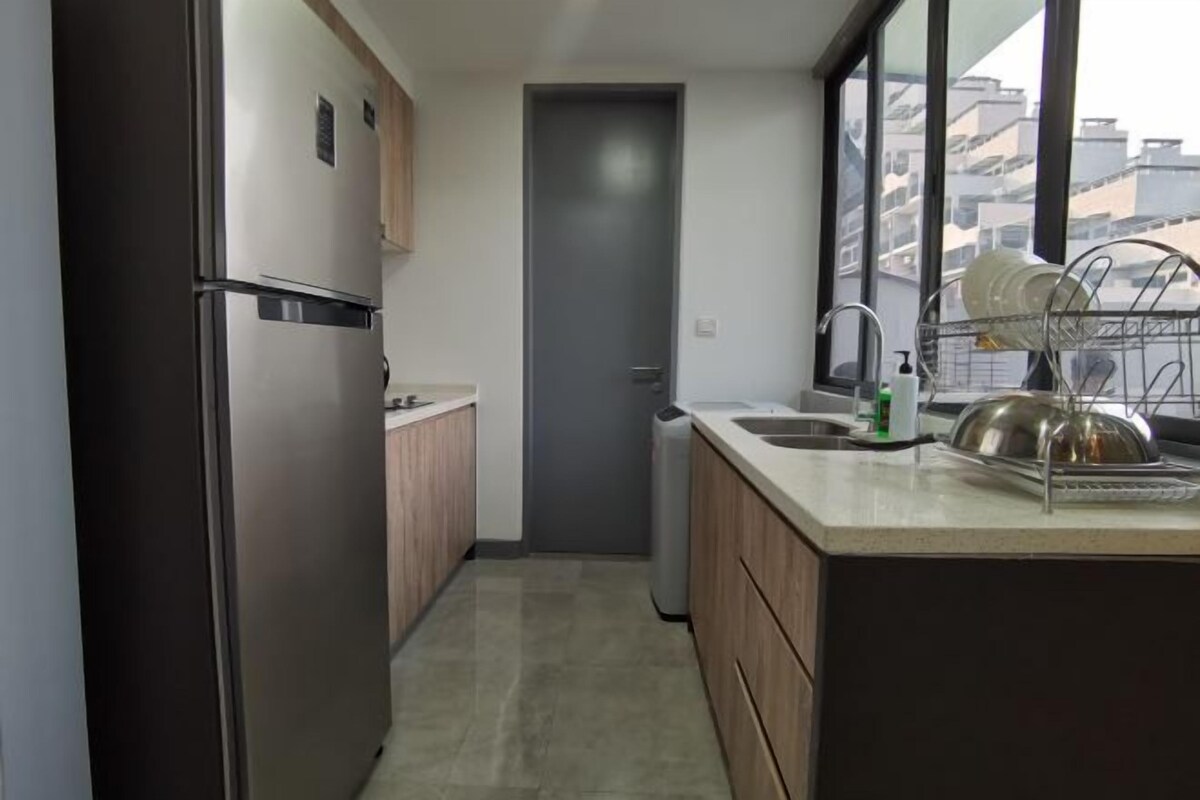 A modern kitchen with a stainless steel refrigerator, wooden cabinets, a built-in dishwasher, and a window providing a view of the cityscape.