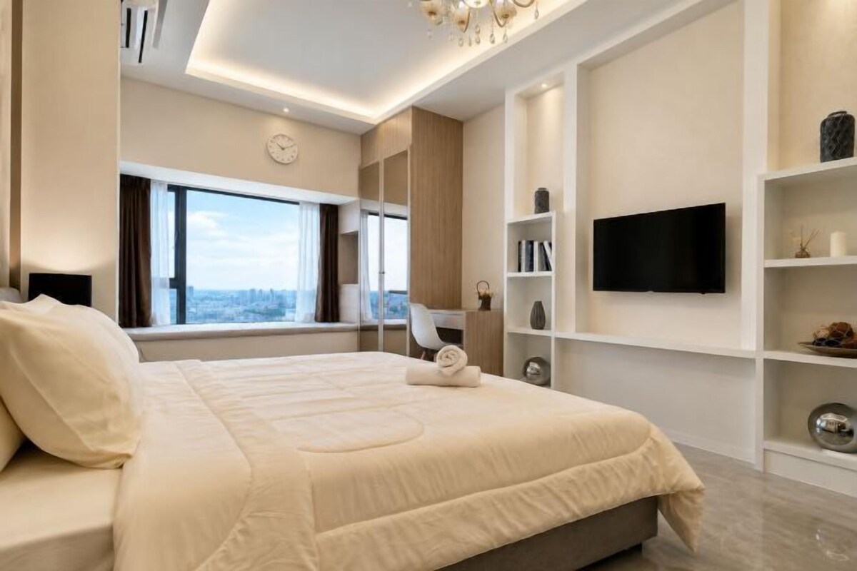 A modern bedroom with a large bed, a TV, and a city view.