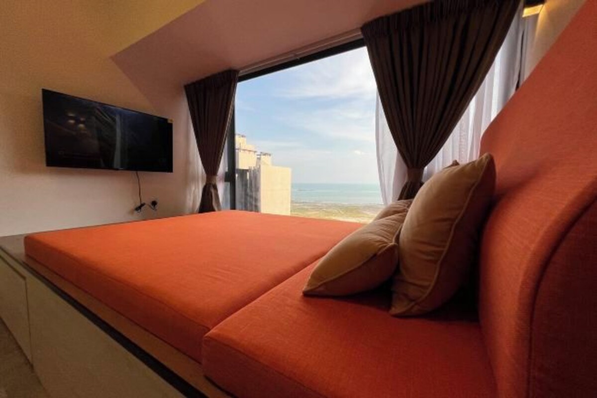 A hotel room with a bed, a TV mounted on the wall, and a view of the sea.