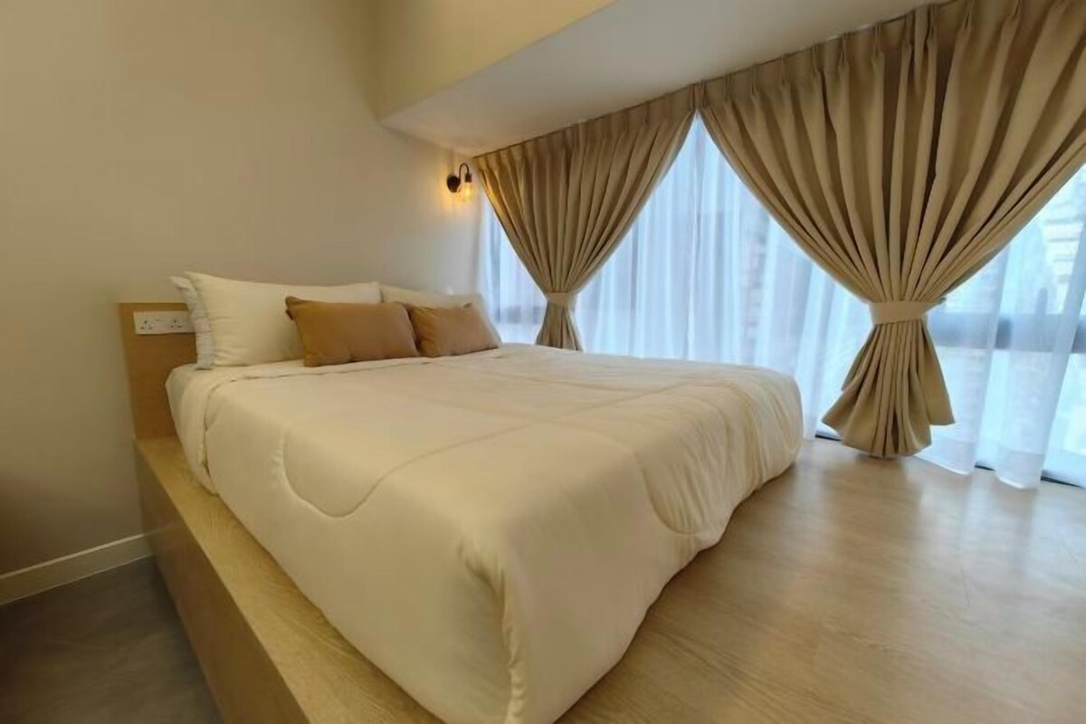 A hotel room with a large bed, beige curtains, and a wooden floor.