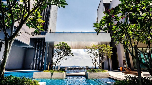 A modern pool area with a clear view of the sea, surrounded by lush greenery and contemporary architecture. - Attic Home Melaka Imperio Residence (Malacca City)